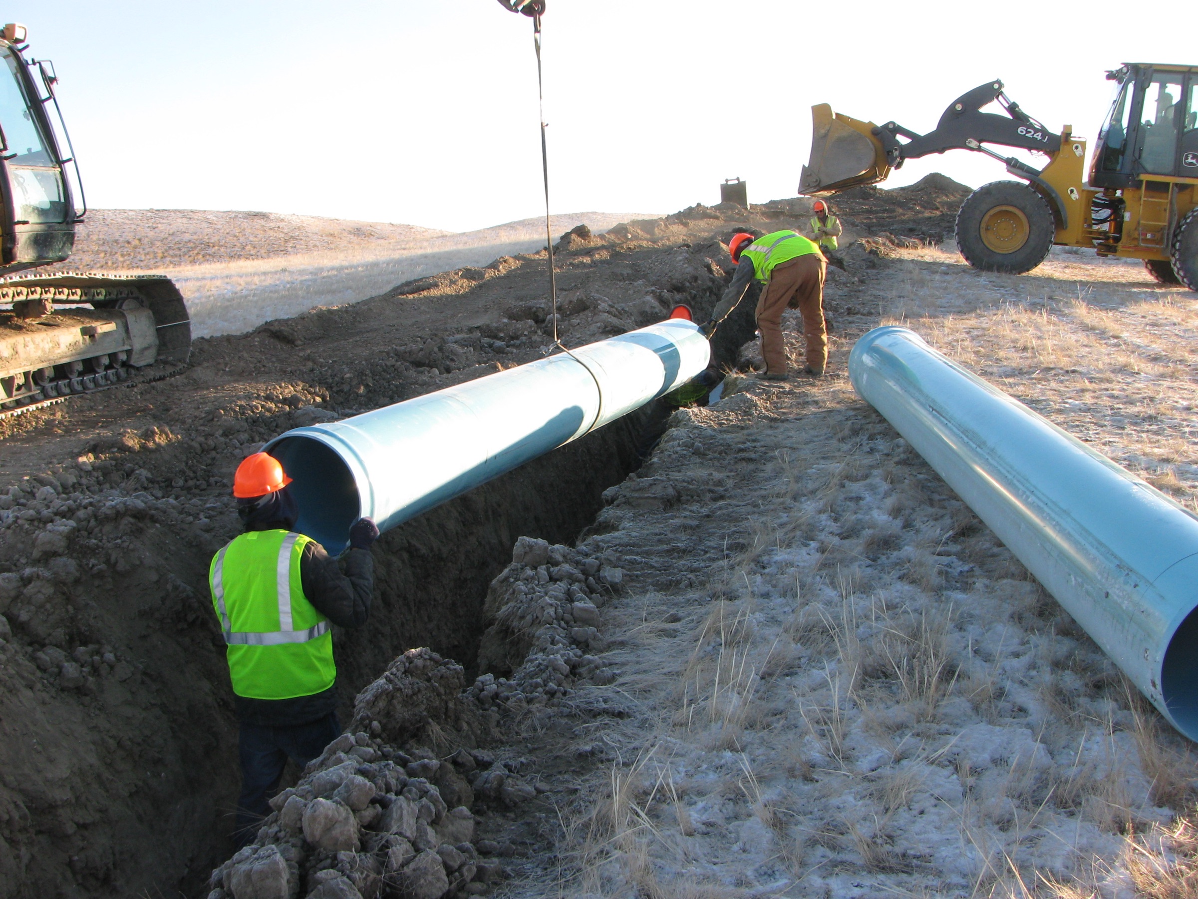 A pipeline being lowered into an open trench by a crew